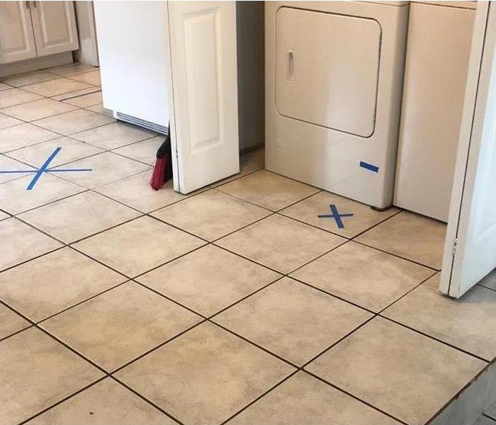 Photo of a washing machine, there are two "X" on the floor marking where the machine caused water damage