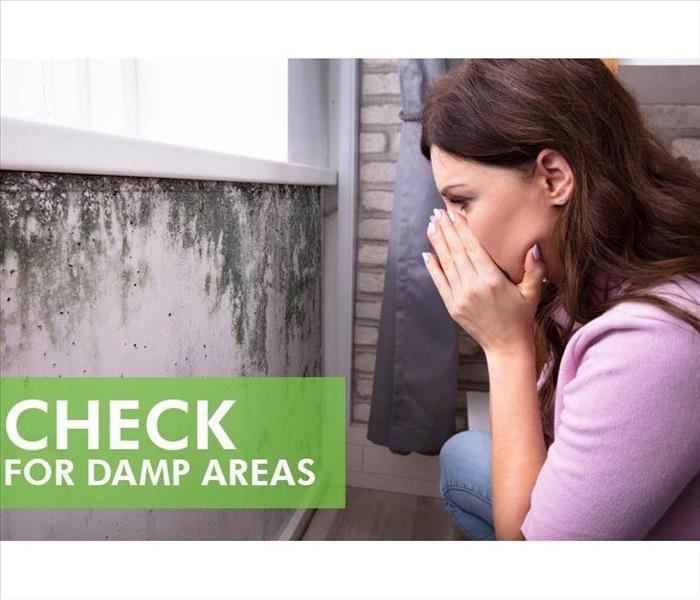 Woman covering her nose while looking at wall with black mold